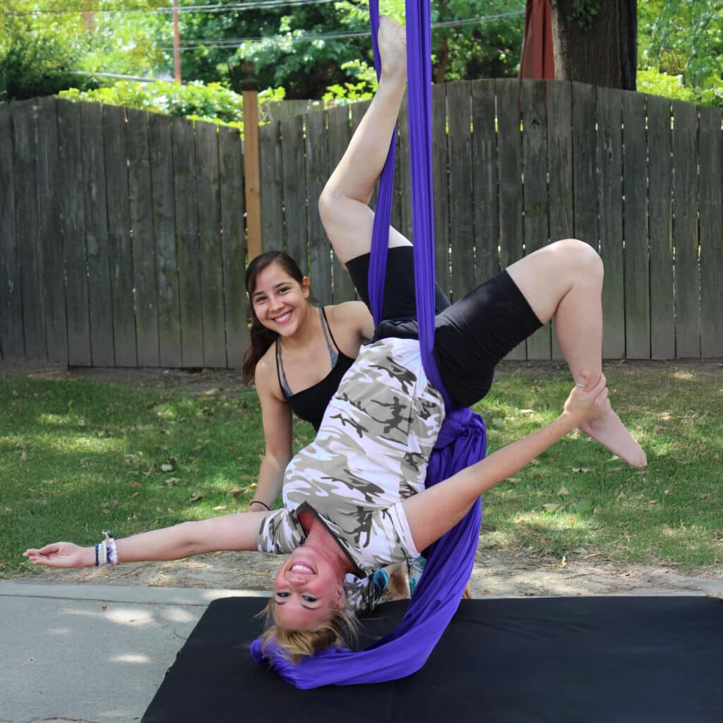 Elevated aerial silk performance with smiling young women outdoors for entertainment.